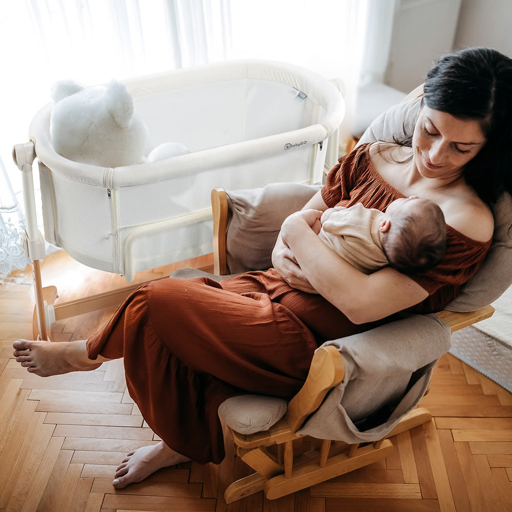 Mutti mit Baby im Schaukelstuhl neben einem Bestellbett